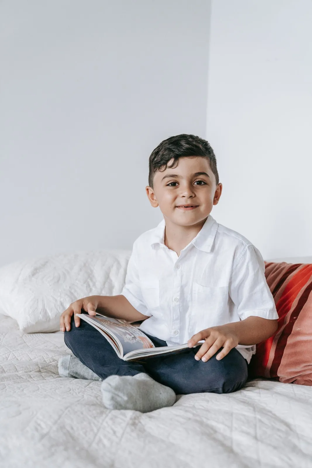 Niño sonriente sentado en su cama con un libro abierto