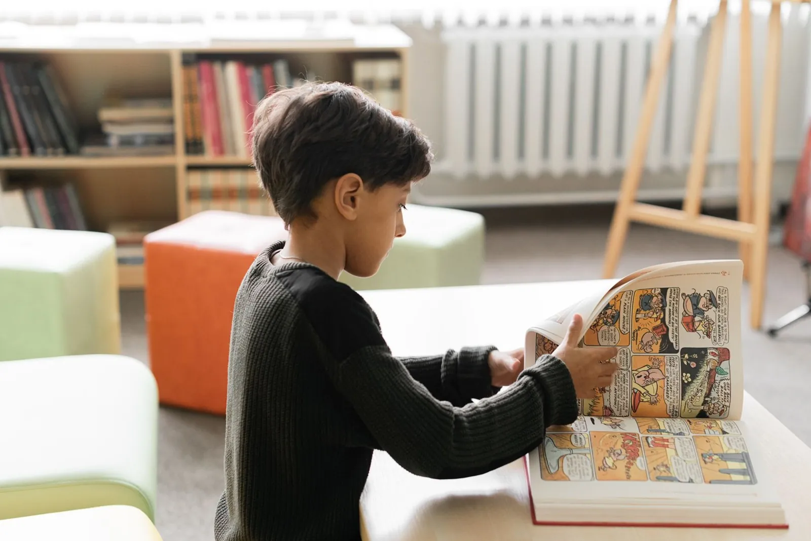 Niño da vuelta la página de un libro de cómics sobre la mesa de la biblioteca de su casa