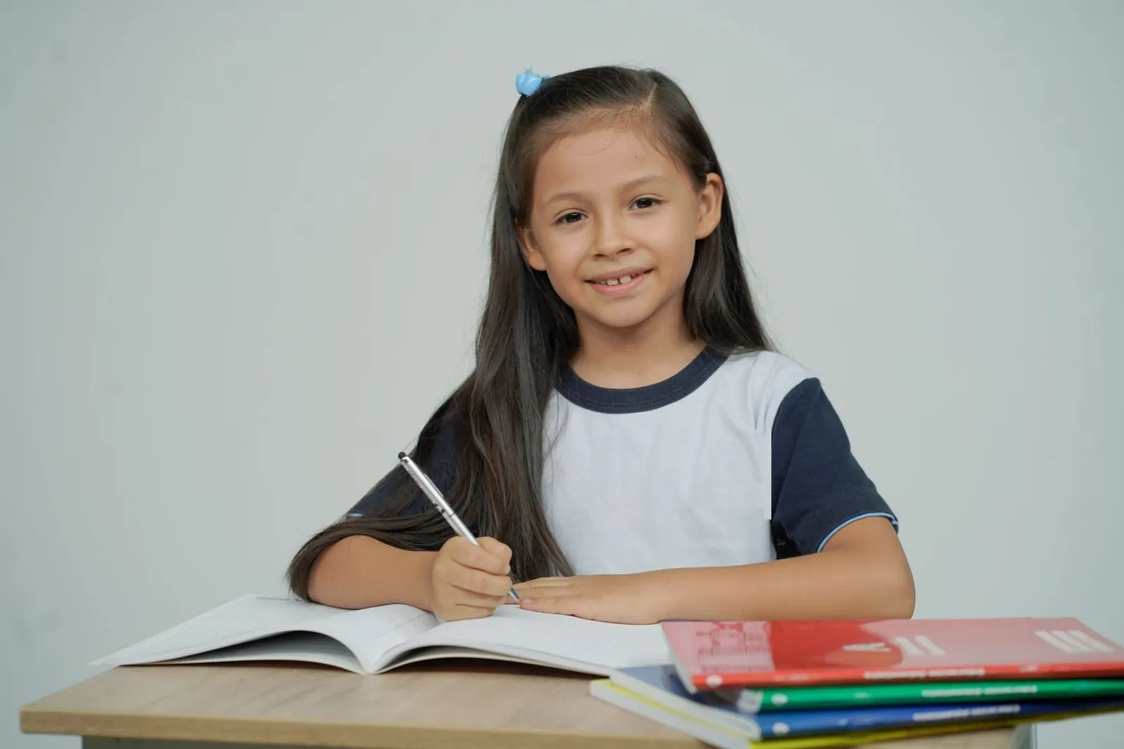 Niña sonríe sentada en su escritorio, con cuadernos y libros abiertos